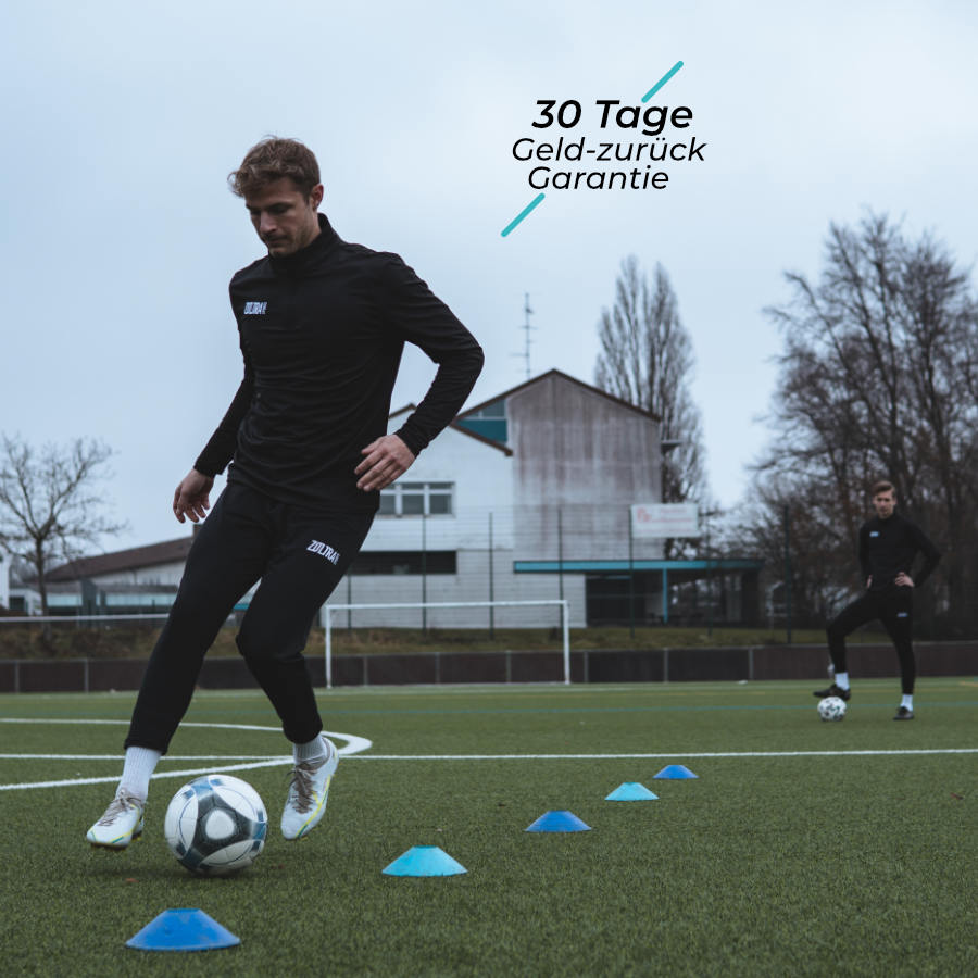 Eine Fußballer dribbelt mit einem Ball durch blaue Hütchen. Auf seiner Hose und seinem Pulli steht jeweils Zoltra Sports. Im Hintergrund ist ein weiterer Fußballer und ein Tor zu sehen. Rechts oben steht ein Text mit 30 Tage Geld-zurück-Garantie.