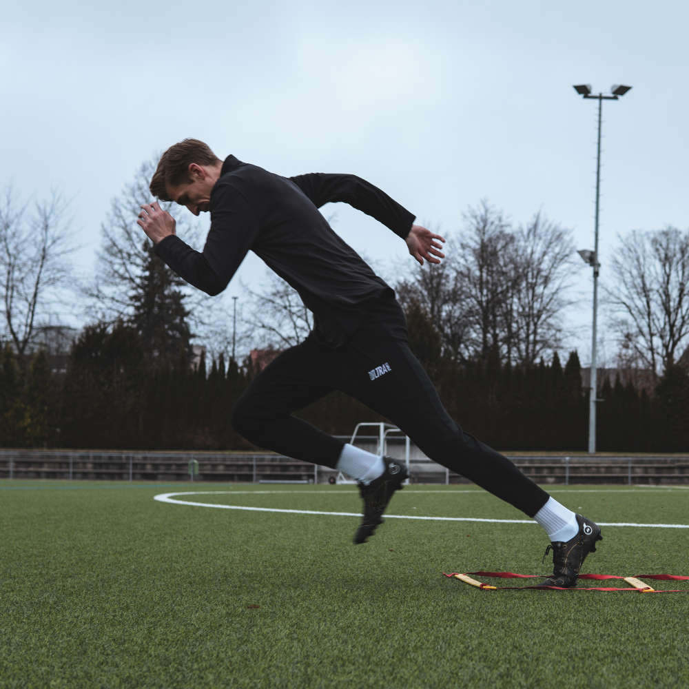 Ein Mensch mit Zoltra Sports Hose auf dem Fußballplatz. Die Person setzt gerade zum Sprint an.